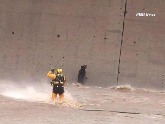 A rescuer wades through fast-moving water to save a dog that had been trapped in the river for nearly two hours.