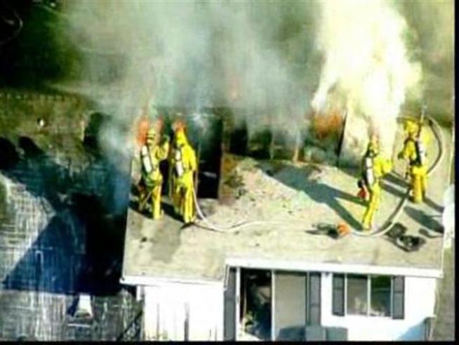 Firefighters attack a house fire from the roof of a <a title=