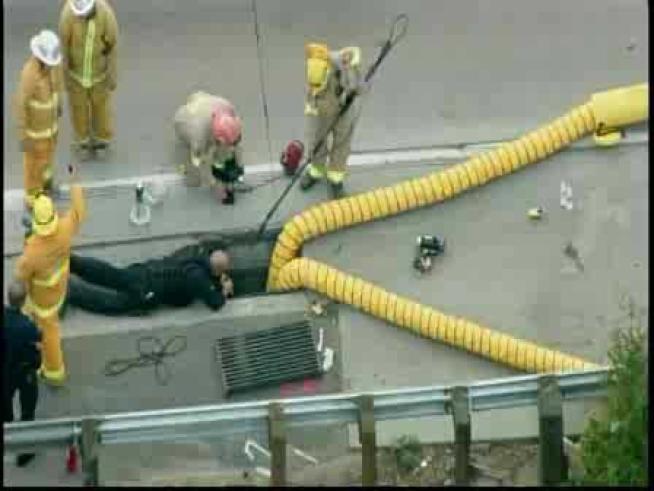 Firefighters work to rescue a suspect trapped inside a drainage area.