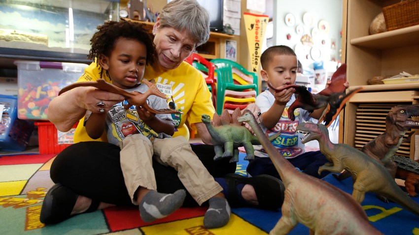 Child care provider Pat Alexander helps children, Isaiah, left, and Hector, right, identify various types of dinosaurs at her child care center in Elk Grove, Calif., on Wednesday, Feb. 26, 2020.