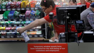 Garrett Ward sprays disinfectant on a conveyor belt between checking out shoppers behind a plexiglass panel at a Hy-Vee grocery store in Overland Park, Kan.