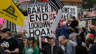 Demonstrators display flags and placards during a protest, Monday, May 4, 2020, in front of the Statehouse, in Boston