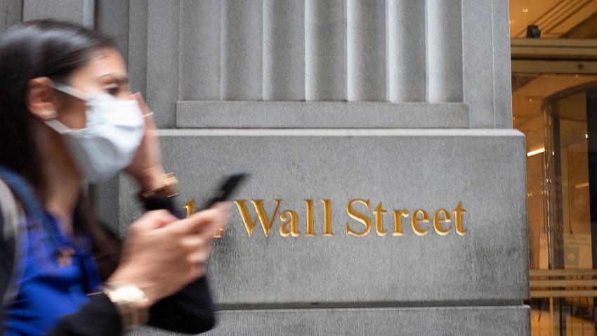 A woman wearing a mask passes a sign for Wall Street, Tuesday, June 30, 2020, during the coronavirus pandemic.