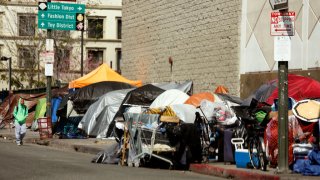 A man walks along a row of tents and enclosures in skid row on March 26, 2020.