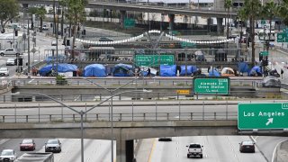 A man rides a bike past tents on an overpass above a freeway.