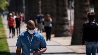 A man wearing a protective mask looks at a mobile phone in front of the California State Capital building in Sacramento, California, U.S., on Tuesday, April 14, 2020.