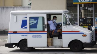 A U.S. Postal Service mail carrier wearing a protective mask closes a vehicle door after refueling in Hawthorne, California, on April 20, 2020.