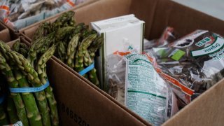 Asparagus and packaged food items are placed in a cardboard box.
