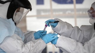 Health workers dressed in personal protective equipment (PPE) handle a coronavirus test at a drive-thru testing station.(Photo by John Moore/Getty Images)