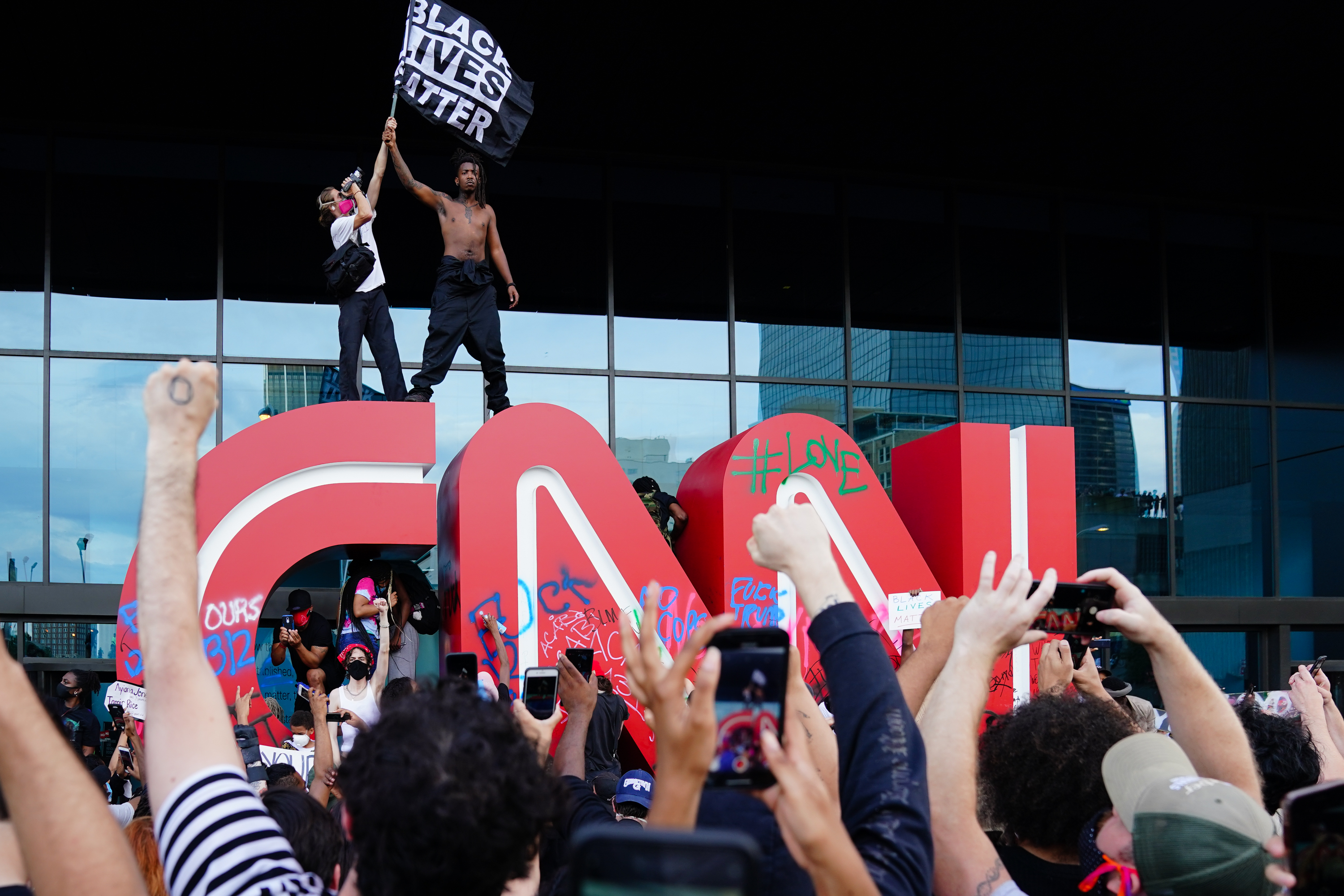 A man waves a Black Lives Matter flag atop the CNN logo during a protest in response to the police killing of George Floyd outside the CNN Center on May 29, 2020, in Atlanta, Georgia.