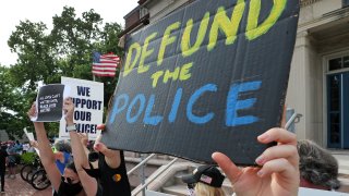 BOSTON, MA – JUNE 4: A person holding a sign reading “defund the police” stands next to a counter protester holding a “we support our police sign” in front of the Newton Police Headquarters in Newton, MA on June 4, 2020. Protesters gather and march calling for justice for George Floyd and other Black Americans killed by police officers on the day of Floyd’s funeral. (Photo by Jim Davis/The Boston Globe via Getty Images)