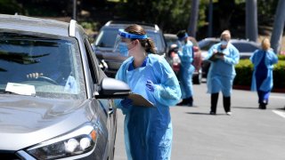 In this April 24, 2020, file photo, workers wearing personal protective equipment (PPE) perform drive-up COVID-19 testing administered from a car at Mend Urgent Care testing site for the coronavirus at the Westfield Culver City.