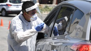 A worker wearing personal protective equipment (PPE) performs COVID-19 test on driver in car