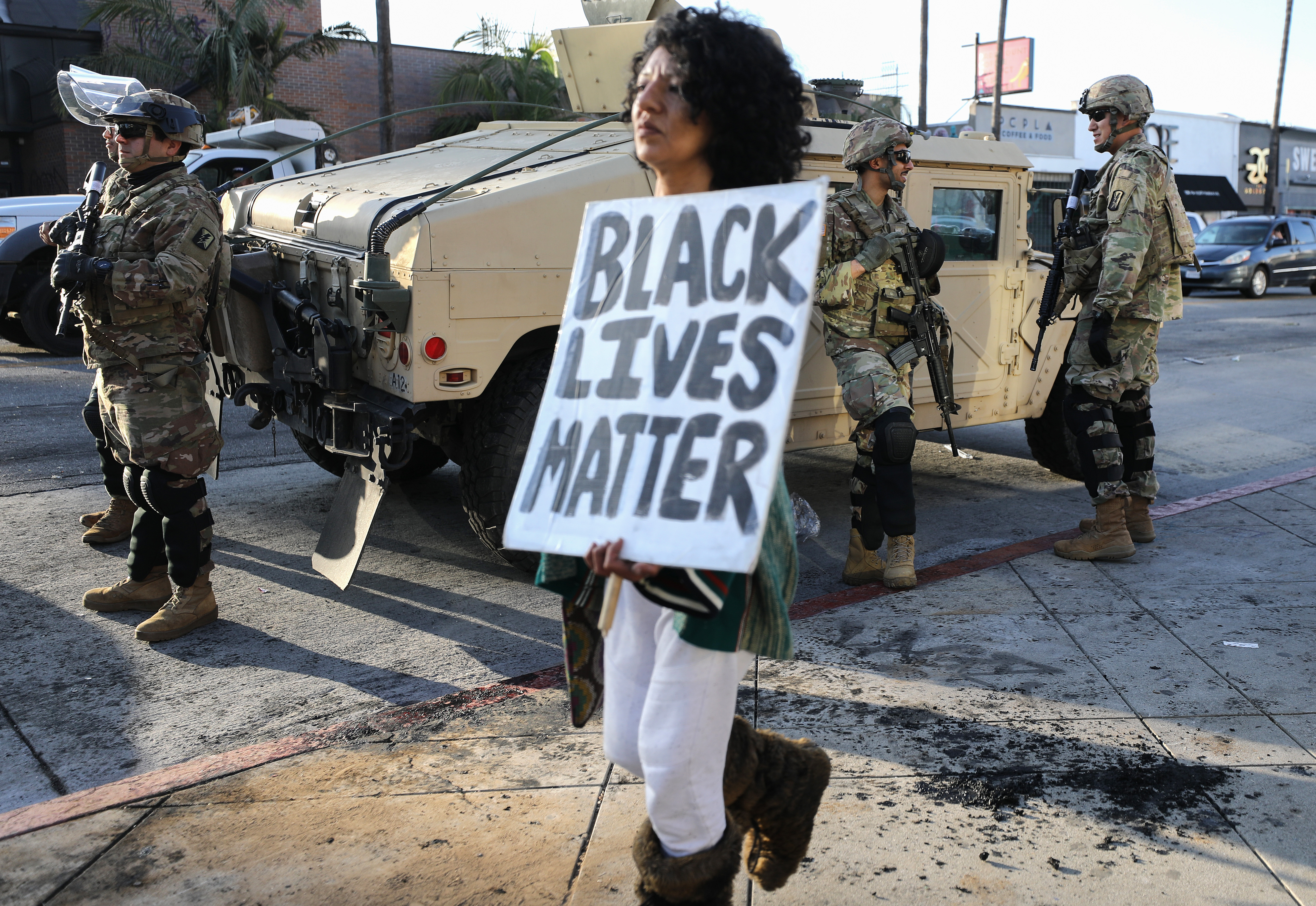 A woman carries a ‘Black Lives Matter’ sign past U.S. National Guard troops in the Fairfax District, an area damaged during yesterday’s unrest, after the troops were activated by California Governor Gavin Newsom following violent demonstrations in response to George Floyd’s death on May 31, 2020, in Los Angeles, California.