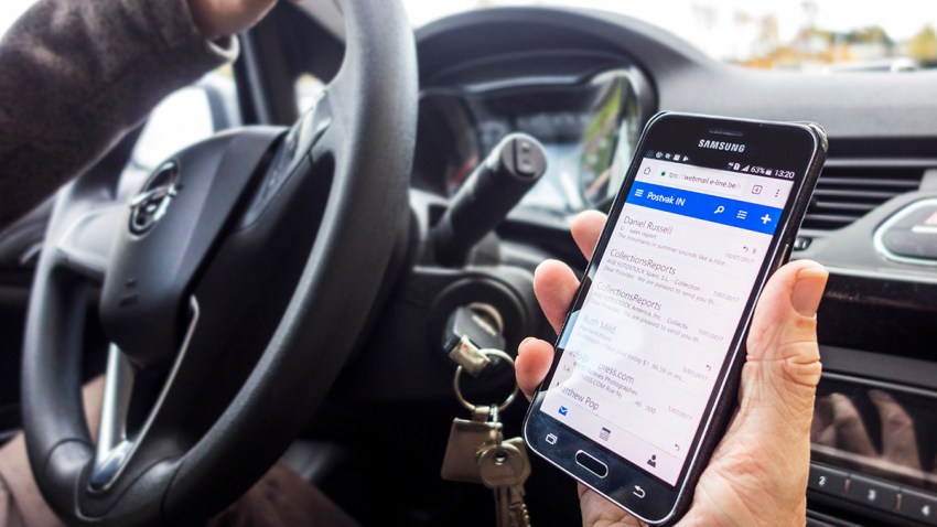 Man at steering wheel checks messages on smartphone