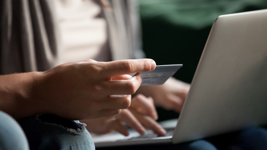 付款和网上购物的概念，一对夫妇用电脑进行网上购物，客户通过电子银行服务在笔记本电脑上进行安全支付，手拿信用卡的近景。(photo:NBCLA)