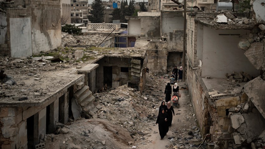 In this Thursday, March 12, 2020 photo, women walk in a neighborhood heavily damaged by airstrikes in Idlib, Syria.