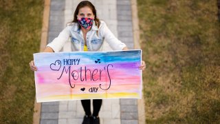 Woman with mask holds up a sign that says "Happy Mothers Day"