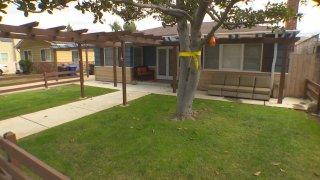 A one-story home with a green lawn and a tree with a yellow ribbon tied around it