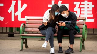 People wearing face masks to protect against the spread of the new coronavirus sit on a bench in front of a propaganda banner encouraging people to wear masks at a public park in Beijing, Thursday, May 7, 2020.