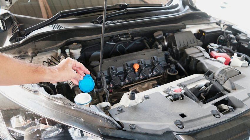 Close up of mechanic’s arm checking at car engine front hood open. Auto mechanic inspecting car engine.