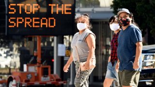 FILE – Pedestrians wear masks as they walk in front of a sign reminding the public to take steps to stop the spread of coronavirus, Thursday, July 23, 2020, in Glendale, Calif. After weeks of stressing education over enforcement, California communities say they are now issuing fines and relying on anonymous tips to make sure businesses and residents are complying with health orders requiring masks, disinfection, and social distancing as the state tries to contain the coronavirus. (AP Photo/Chris Pizzello, File)