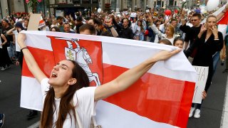 A woman reacts as she marches holding an old Belarusian national flag in the center of Minsk, Belarus, Friday, Aug. 14, 2020. Some thousands of people have flooded the cnetre of the Belarus capital, Minsk, in a show of anger over a brutal police crackdown this week on peaceful protesters that followed a disputed election.