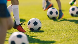 People dribble soccer balls on a green pitch.