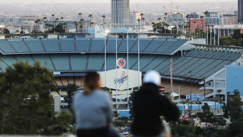 People sit on a hill overlooking Dodger Stadium on what was supposed to be Major League Baseball’s opening day, now postponed due to the coronavirus, on March 26, 2020 in Los Angeles, California. The Los Angeles Dodgers were slated to play against the San Francisco Giants at the stadium today. Major League Baseball Commissioner Rob Manfred recently said the league is “probably not gonna be able to” play a full 162 game regular season due to the spread of COVID-19. (Photo by Mario Tama/Getty Images)