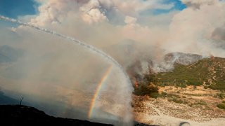 Water from a fire engine creates a rainbow near flames as firefighters continue to battle the Apple fire near Banning, California on August 1, 2020. – 4,125 acres have burn in Cherry Valley, about 2,000 people have received evacuation orders in the afternoon of August 1.
Around 8PM the fire spread to 12,000 acres. (Photo by JOSH EDELSON / AFP) (Photo by JOSH EDELSON/AFP via Getty Images)