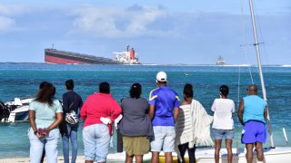 Bystanders look at MV Wakashio bulk carrier that had run aground and from which oil is leaking near Blue Bay Marine Park in south-east Mauritius on August 6, 2020.