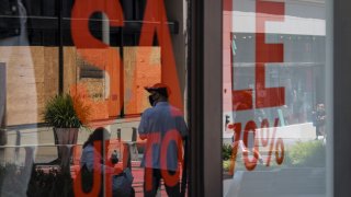 People wearing protective masks walk past an H&M store window display in San Francisco, California, U.S., on Thursday, Aug. 6, 2020. U.S. consumer sentiment extended its slide in late July as the resurgent coronavirus led to renewed business closings and layoffs, adding to signs the economic recovery is stalling.