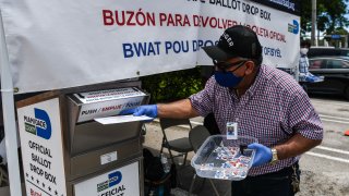 In this Aug. 18, 2020, file photo, poll workers help a voter put their mail-in ballot in an official Miami-Dade County drive- thru ballot drop box during Florida Primary Election amid the coronavirus pandemic, in Miami, Florida.