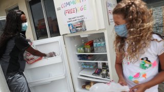 Sherina Jones (L) helps Valentina Pedon, 9, place the items her family is donating into the community refrigerator she set up in front of the Roots Collective store on August 21, 2020 in Miami, Florida. The fridge is set up to help people who need food, especially people who have lost jobs during the coronavirus (COVID-19) pandemic.