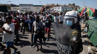 Migrants take part in a rally as riot police block the road near Mytilene town