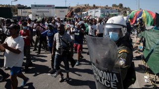 Migrants take part in a rally as riot police block the road near Mytilene town