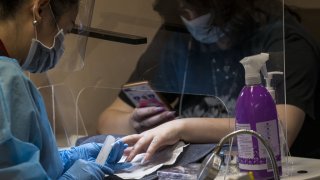 A worker wearing personal protective equipment (PPE) helps a customer wearing a protective mask at a nail salon in Palo Alto, California, U.S., on Tuesday, July 14, 2020. Governor Newsom pulled back on reopening efforts, banning indoor restaurant dining throughout the state and ordering a halt to indoor activities at gyms, hair salons and places of worship in the state’s 30 most affected counties. Photographer: David Paul Morris/Bloomberg via Getty Images