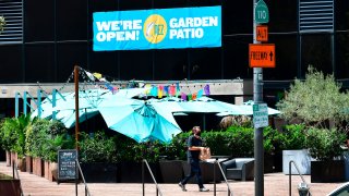 A man carries his takeout order past umbrellas covering an outdoor patio dining area in Los Angeles.