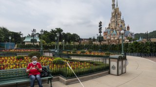 A visitor sits at a bench next to a white cord as he waits for the park to be open at the Disneyland Resort in Hong Kong, China on September 25, 2020.