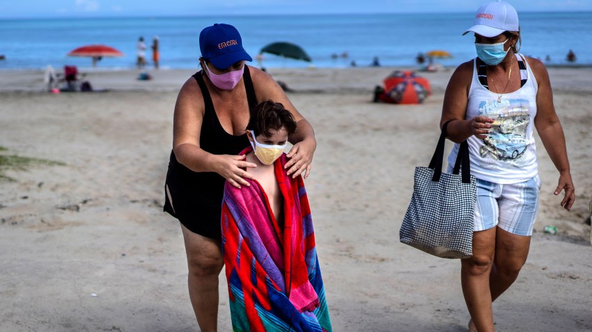 Wearing a mask as a precaution against the spread of the new coronavirus, a woman towels off a child at a beach in Havana, Cuba, Sunday, Oct. 11, 2020.