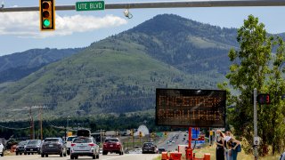 Pedestrians walk in front of a street sign that reads "Face Mask Requried" in Summit County near Park City, Utah