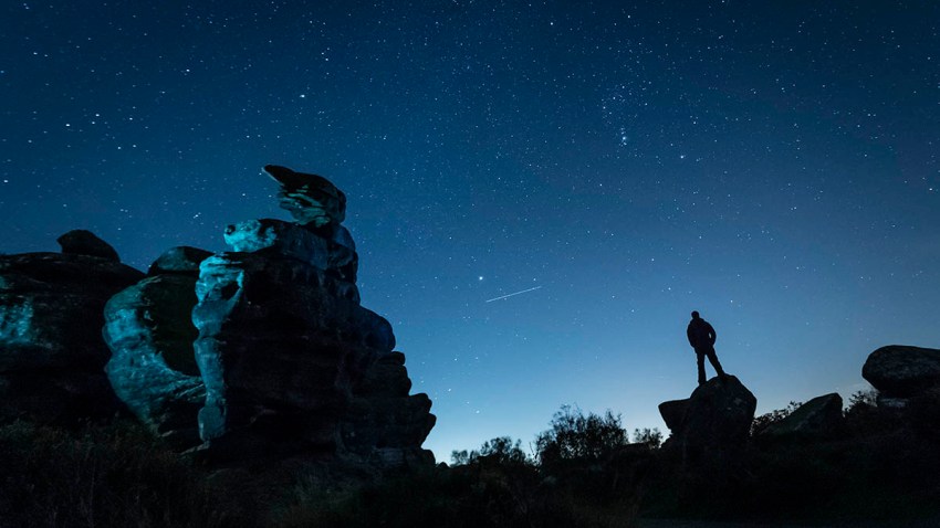 An airplane flies in the night sky above a stargazer amid the Orionid meteor shower at Brimham Rocks in Yorkshire, England, Oct. 22, 2018.