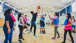 Two kids in a gym jump up to grab for a basketball in the air