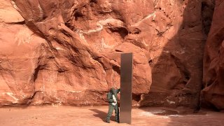 This Nov. 18, 2020, photo provided by the Utah Department of Public Safety shows a Utah state worker inspecting a metal monolith that was found installed in the ground in a remote area of red rock desert in Utah. The smooth, tall structure was found during a helicopter survey of bighorn sheep in southeastern Utah, officials said Monday.