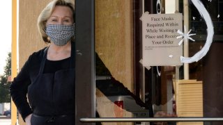 Brenda Luntey, poses for a photo by a sign advising customers to wear face masks that is posted on the door of the San Francisco Deli in Redding, Calif., Thursday, Dec. 3, 2020.