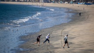 File Image: People wearing masks exercise on the beach in Long Beach Thursday, Dec. 10, 2020. (Allen J. Schaben / Los Angeles Times via Getty Images)