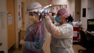 Registered nurse Dania Lima, right, helps fellow nurse Adriana Volynsky put on her personal protective equipment in a COVID-19 unit at Providence Holy Cross Medical Center in the Mission Hills section of Los Angeles, Tuesday, Dec. 22, 2020.