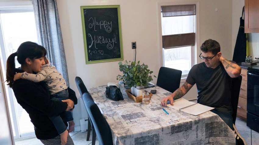 Comedian Brad Pierce, right, looks over the notebook us uses to write jokes as he sits in the kitchen next to his wife, Carmen, and their nephew, Maddox, 1, in West Warwick, R.I.