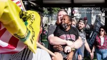 A woman is wrapped in a bear-hug by a man in a hostile crowd during a rally.