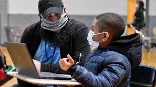 In this Jan. 19, 2021, file photo, Jordan Rodriguez, director of the Mulberry Street club, works with Santana Sanford, 7, a second grade student, as he does his school work on a laptop computer.